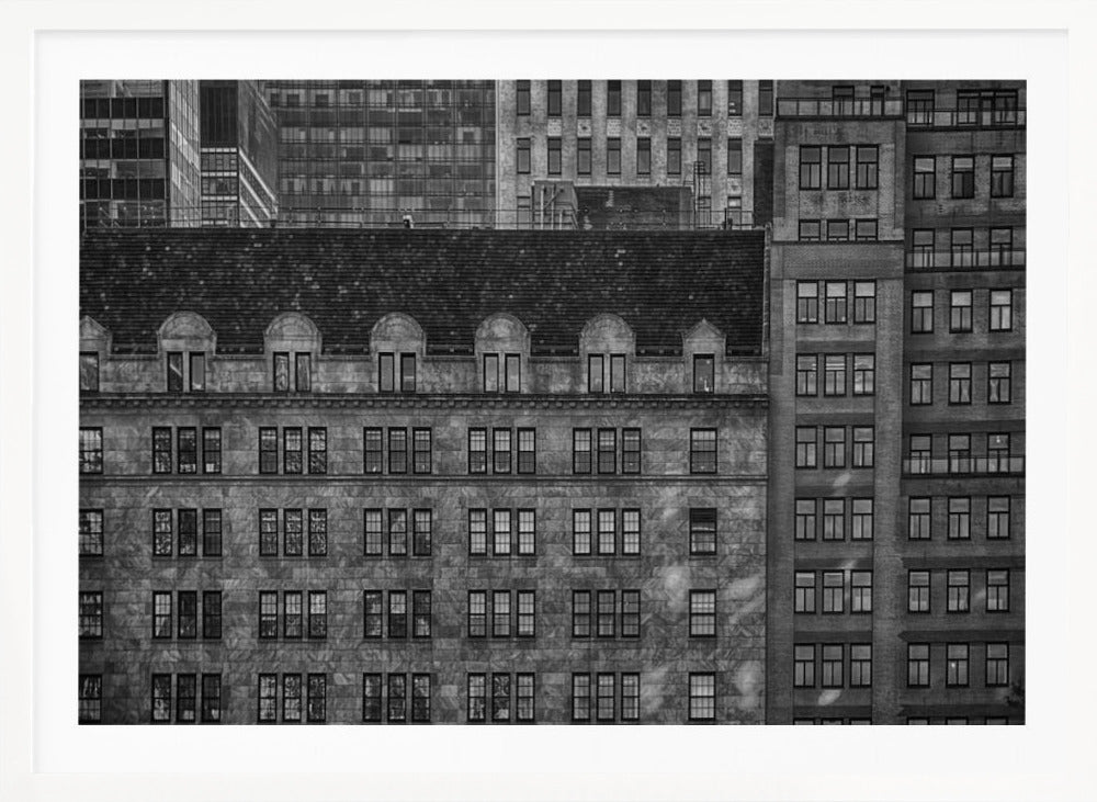 A dense, black and white photograph of various city buildings packed closely together. The image highlights the contrasting architectural styles, from an older stone building with a dark roof in the foreground to taller brick and modern glass buildings in the background, creating a geometric pattern of windows and textures. Decor
