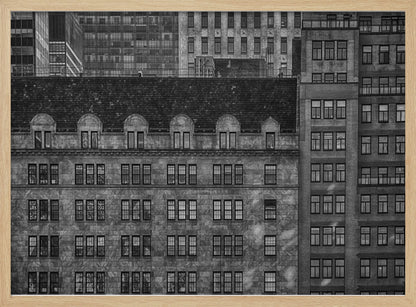 A dense, black and white photograph of various city buildings packed closely together. The image highlights the contrasting architectural styles, from an older stone building with a dark roof in the foreground to taller brick and modern glass buildings in the background, creating a geometric pattern of windows and textures. Decor