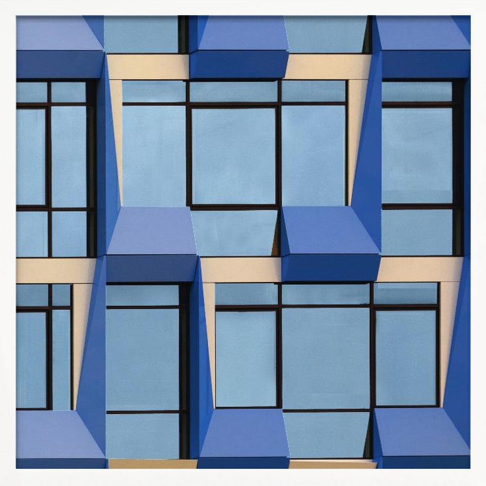 A framed abstract architectural photograph showing a repeating pattern of a modern building's facade. The image features geometric, three-dimensional blue elements surrounding light blue windows with black frames, all set against horizontal cream-colored bands. The entire piece is presented within a light wood frame. Print
