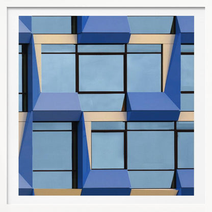 A framed abstract architectural photograph showing a repeating pattern of a modern building's facade. The image features geometric, three-dimensional blue elements surrounding light blue windows with black frames, all set against horizontal cream-colored bands. The entire piece is presented within a light wood frame. Print