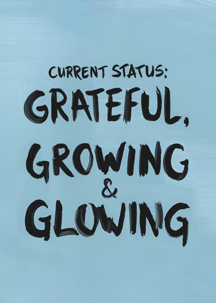 A motivational poster with a light blue background and a thin black frame. The text 'CURRENT STATUS: GRATEFUL, GROWING & GLOWING' is written in a bold, black, handwritten brush font. Decor