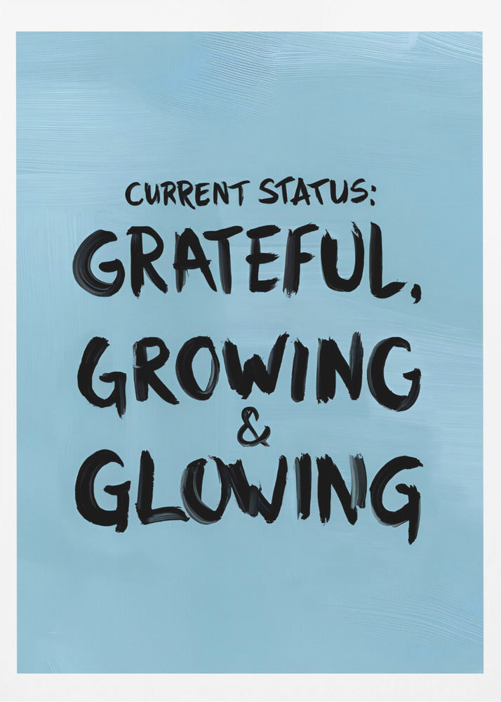 A motivational poster with a light blue background and a thin black frame. The text 'CURRENT STATUS: GRATEFUL, GROWING & GLOWING' is written in a bold, black, handwritten brush font. Decor