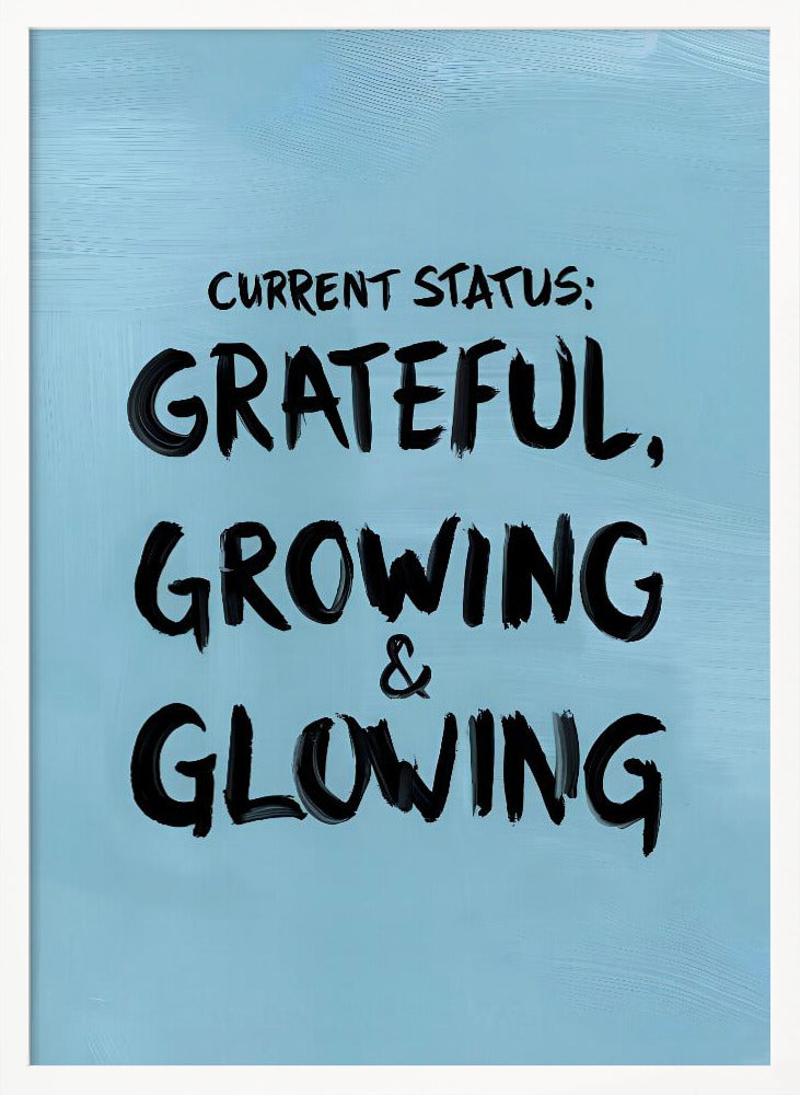 A motivational poster with a light blue background and a thin black frame. The text 'CURRENT STATUS: GRATEFUL, GROWING & GLOWING' is written in a bold, black, handwritten brush font. Decor