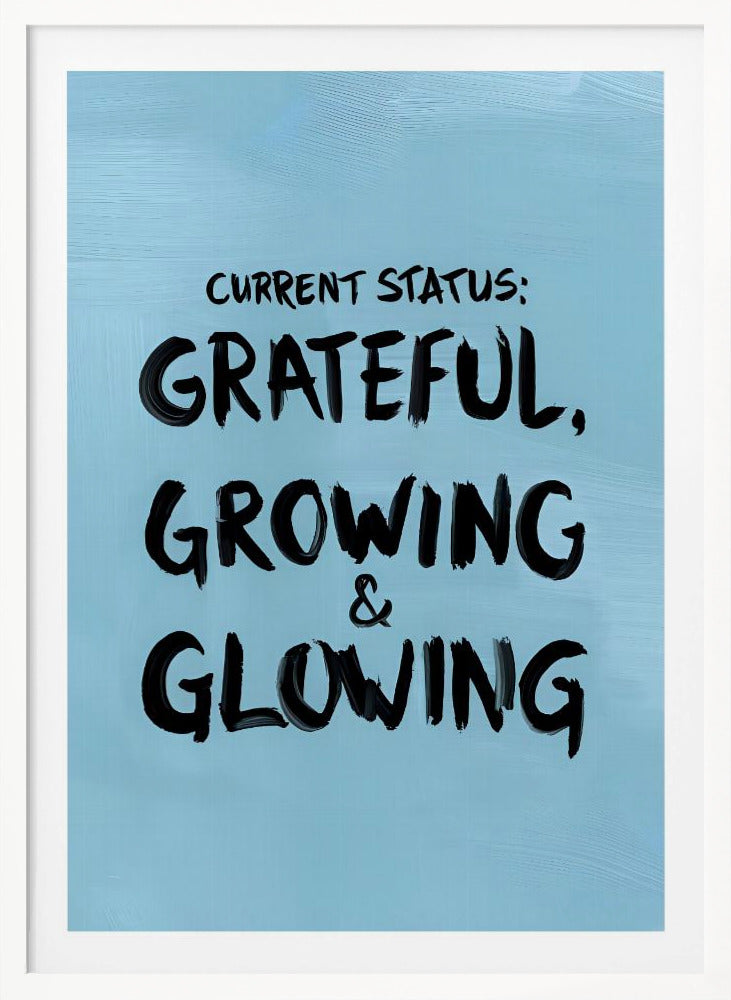 A motivational poster with a light blue background and a thin black frame. The text 'CURRENT STATUS: GRATEFUL, GROWING & GLOWING' is written in a bold, black, handwritten brush font. Decor