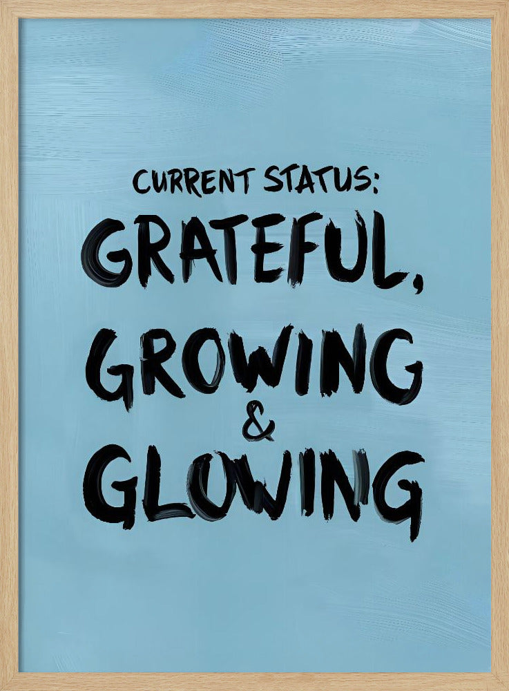 A motivational poster with a light blue background and a thin black frame. The text 'CURRENT STATUS: GRATEFUL, GROWING & GLOWING' is written in a bold, black, handwritten brush font. Decor