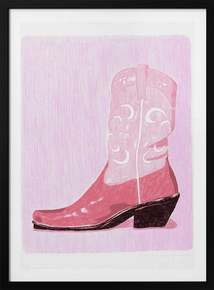 A framed art print of a pink cowboy boot against a light pink, textured background. The boot is illustrated in a block-print style with shades of pink, white decorative inlay patterns of moons and stars, and a dark brown heel and sole. Decor