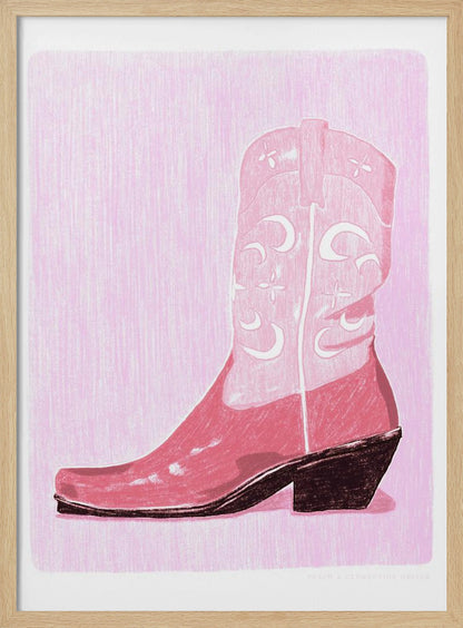 A framed art print of a pink cowboy boot against a light pink, textured background. The boot is illustrated in a block-print style with shades of pink, white decorative inlay patterns of moons and stars, and a dark brown heel and sole. Decor