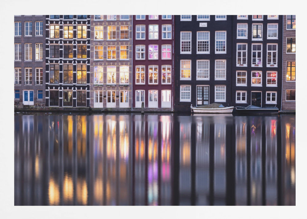 A framed photograph of colorful Amsterdam canal houses at night, their illuminated windows casting vibrant, shimmering reflections on the water below. Artwork