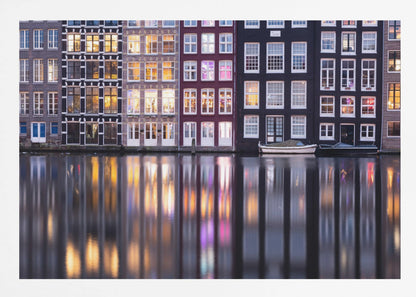 A framed photograph of colorful Amsterdam canal houses at night, their illuminated windows casting vibrant, shimmering reflections on the water below. Artwork