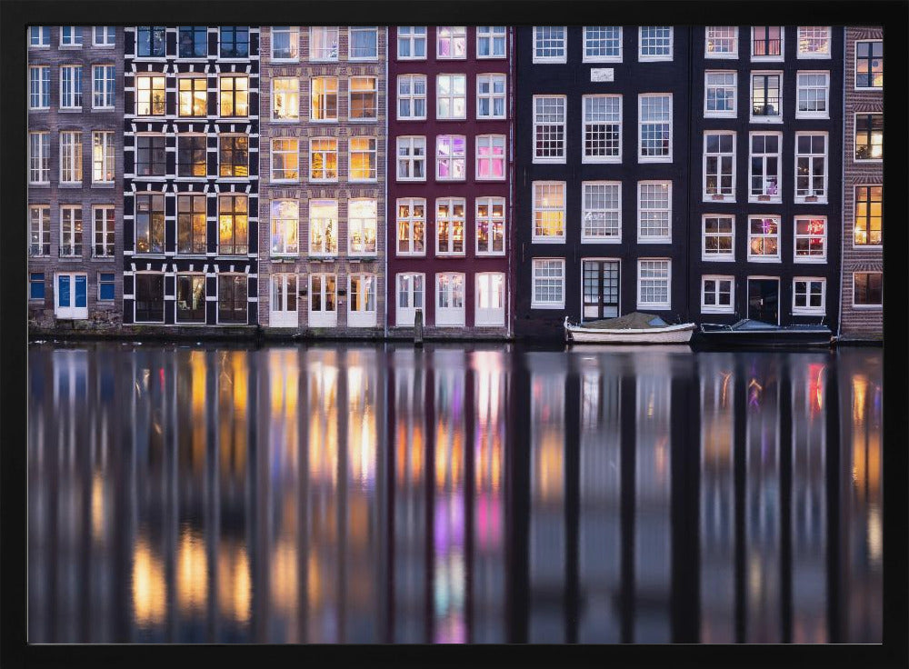 A framed photograph of colorful Amsterdam canal houses at night, their illuminated windows casting vibrant, shimmering reflections on the water below. Artwork