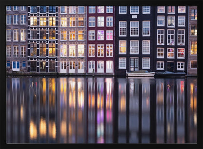 A framed photograph of colorful Amsterdam canal houses at night, their illuminated windows casting vibrant, shimmering reflections on the water below. Artwork