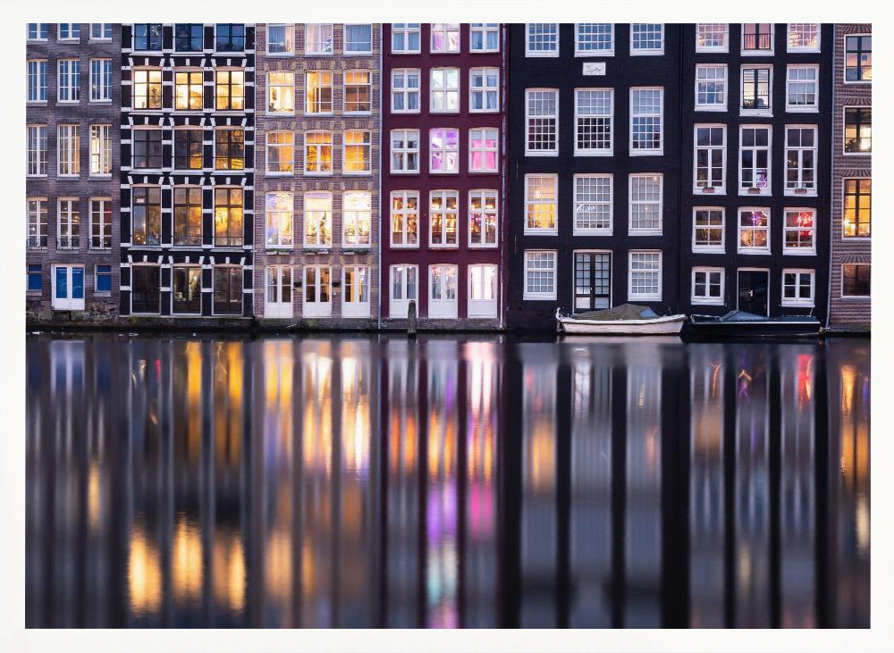 A framed photograph of colorful Amsterdam canal houses at night, their illuminated windows casting vibrant, shimmering reflections on the water below. Artwork