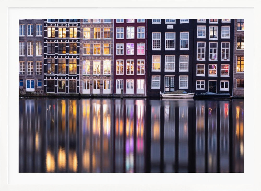 A framed photograph of colorful Amsterdam canal houses at night, their illuminated windows casting vibrant, shimmering reflections on the water below. Artwork