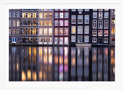 A framed photograph of colorful Amsterdam canal houses at night, their illuminated windows casting vibrant, shimmering reflections on the water below. Artwork