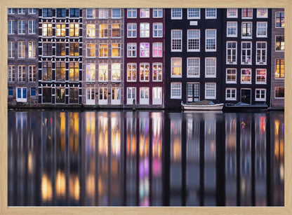 A framed photograph of colorful Amsterdam canal houses at night, their illuminated windows casting vibrant, shimmering reflections on the water below. Artwork
