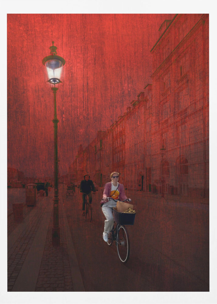 A surreal artistic image of a city street bathed in a textured red light. A woman rides a bicycle with a basket towards the viewer, while another cyclist is in the background. A tall, ornate lamppost is lit on the left side of the cobblestone street. Wall Art