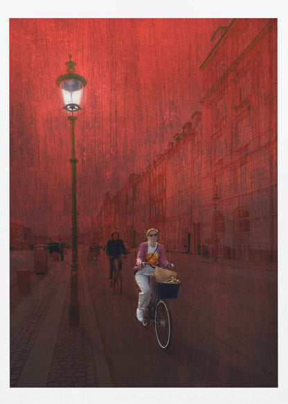 A surreal artistic image of a city street bathed in a textured red light. A woman rides a bicycle with a basket towards the viewer, while another cyclist is in the background. A tall, ornate lamppost is lit on the left side of the cobblestone street. Wall Art