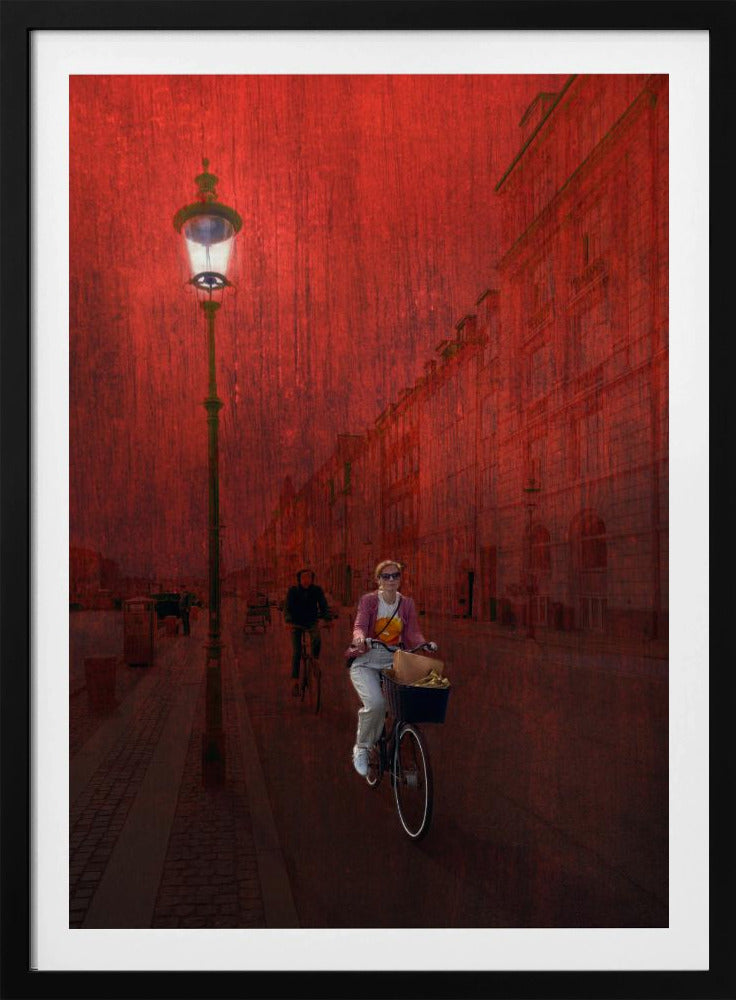 A surreal artistic image of a city street bathed in a textured red light. A woman rides a bicycle with a basket towards the viewer, while another cyclist is in the background. A tall, ornate lamppost is lit on the left side of the cobblestone street. Wall Art