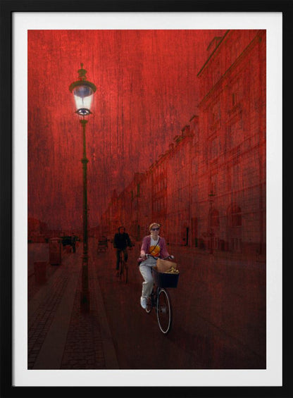 A surreal artistic image of a city street bathed in a textured red light. A woman rides a bicycle with a basket towards the viewer, while another cyclist is in the background. A tall, ornate lamppost is lit on the left side of the cobblestone street. Wall Art