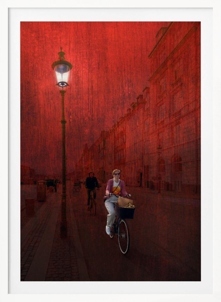 A surreal artistic image of a city street bathed in a textured red light. A woman rides a bicycle with a basket towards the viewer, while another cyclist is in the background. A tall, ornate lamppost is lit on the left side of the cobblestone street. Wall Art