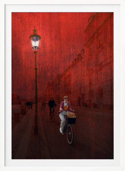 A surreal artistic image of a city street bathed in a textured red light. A woman rides a bicycle with a basket towards the viewer, while another cyclist is in the background. A tall, ornate lamppost is lit on the left side of the cobblestone street. Wall Art