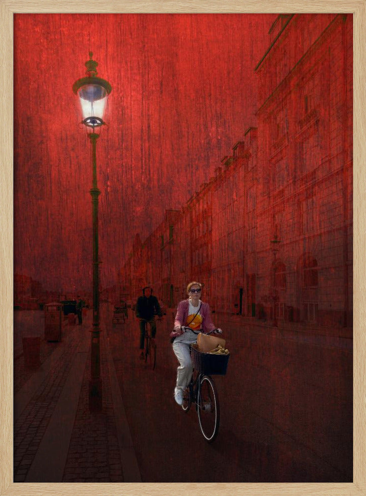 A surreal artistic image of a city street bathed in a textured red light. A woman rides a bicycle with a basket towards the viewer, while another cyclist is in the background. A tall, ornate lamppost is lit on the left side of the cobblestone street. Wall Art