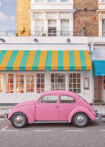 A vibrant, eye-level photograph of a vintage pink Volkswagen Beetle parked on a city street in front of a charming white storefront with a bold yellow and teal striped awning. Wall Art