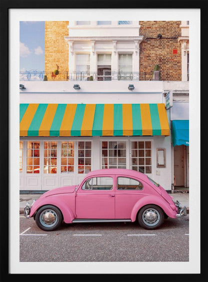 A vibrant, eye-level photograph of a vintage pink Volkswagen Beetle parked on a city street in front of a charming white storefront with a bold yellow and teal striped awning. Wall Art