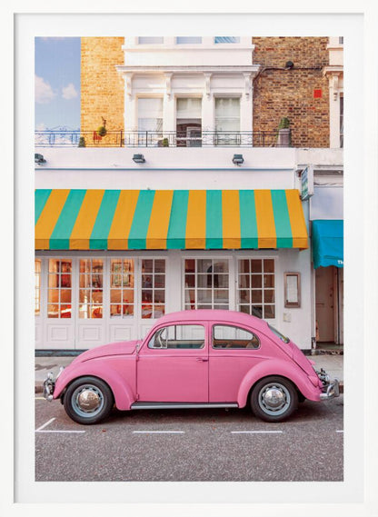 A vibrant, eye-level photograph of a vintage pink Volkswagen Beetle parked on a city street in front of a charming white storefront with a bold yellow and teal striped awning. Wall Art