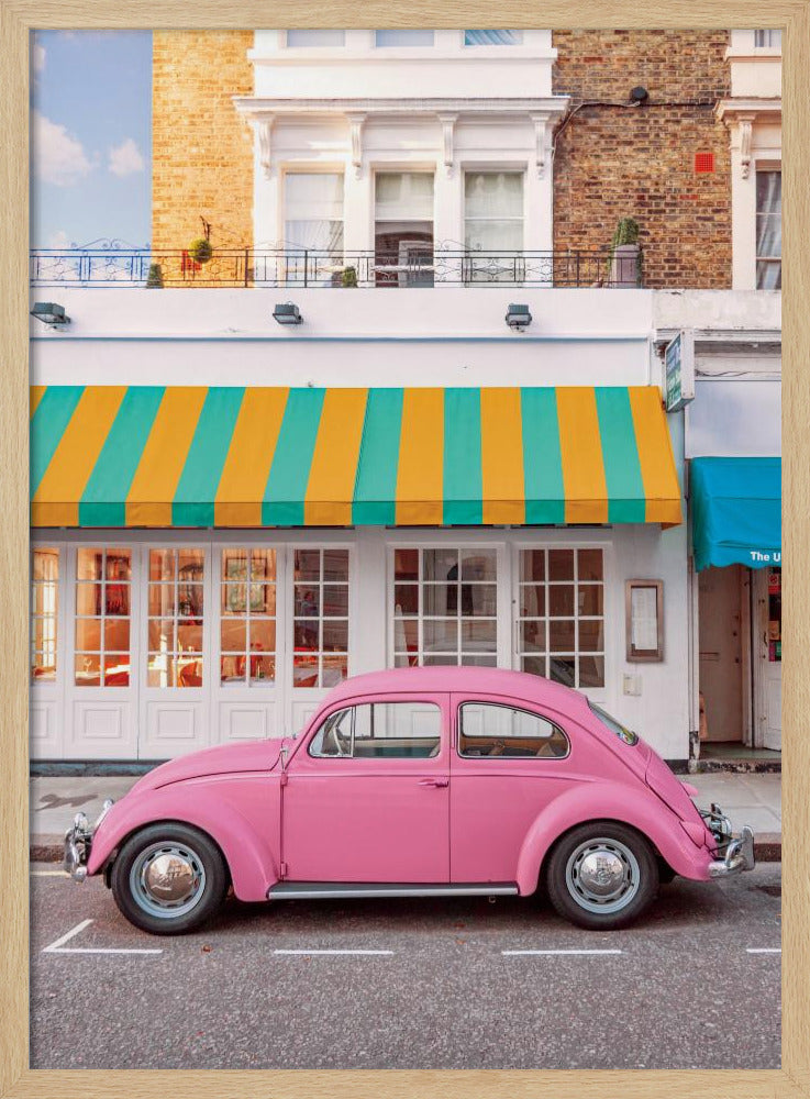 A vibrant, eye-level photograph of a vintage pink Volkswagen Beetle parked on a city street in front of a charming white storefront with a bold yellow and teal striped awning. Wall Art