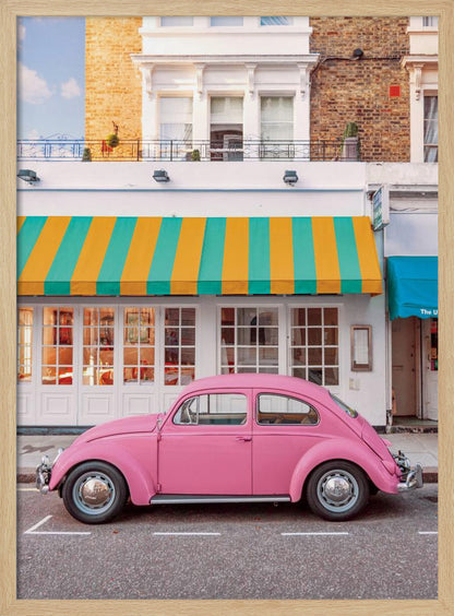 A vibrant, eye-level photograph of a vintage pink Volkswagen Beetle parked on a city street in front of a charming white storefront with a bold yellow and teal striped awning. Wall Art