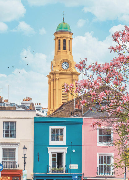 A vibrant city street scene on a sunny day, featuring a row of colorful houses in teal, pink, and off-white. A striking yellow clock tower with a green dome stands tall against a bright blue sky, with a blooming pink magnolia tree in the foreground. Print