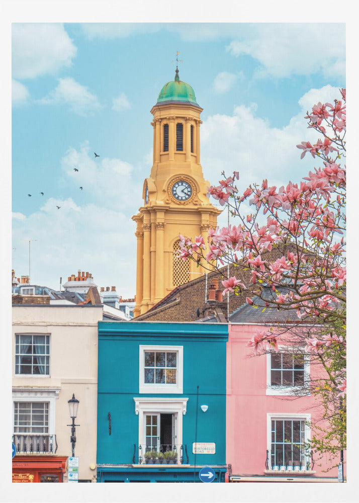 A vibrant city street scene on a sunny day, featuring a row of colorful houses in teal, pink, and off-white. A striking yellow clock tower with a green dome stands tall against a bright blue sky, with a blooming pink magnolia tree in the foreground. Print
