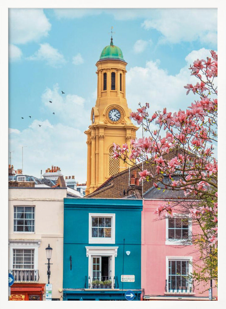 A vibrant city street scene on a sunny day, featuring a row of colorful houses in teal, pink, and off-white. A striking yellow clock tower with a green dome stands tall against a bright blue sky, with a blooming pink magnolia tree in the foreground. Print