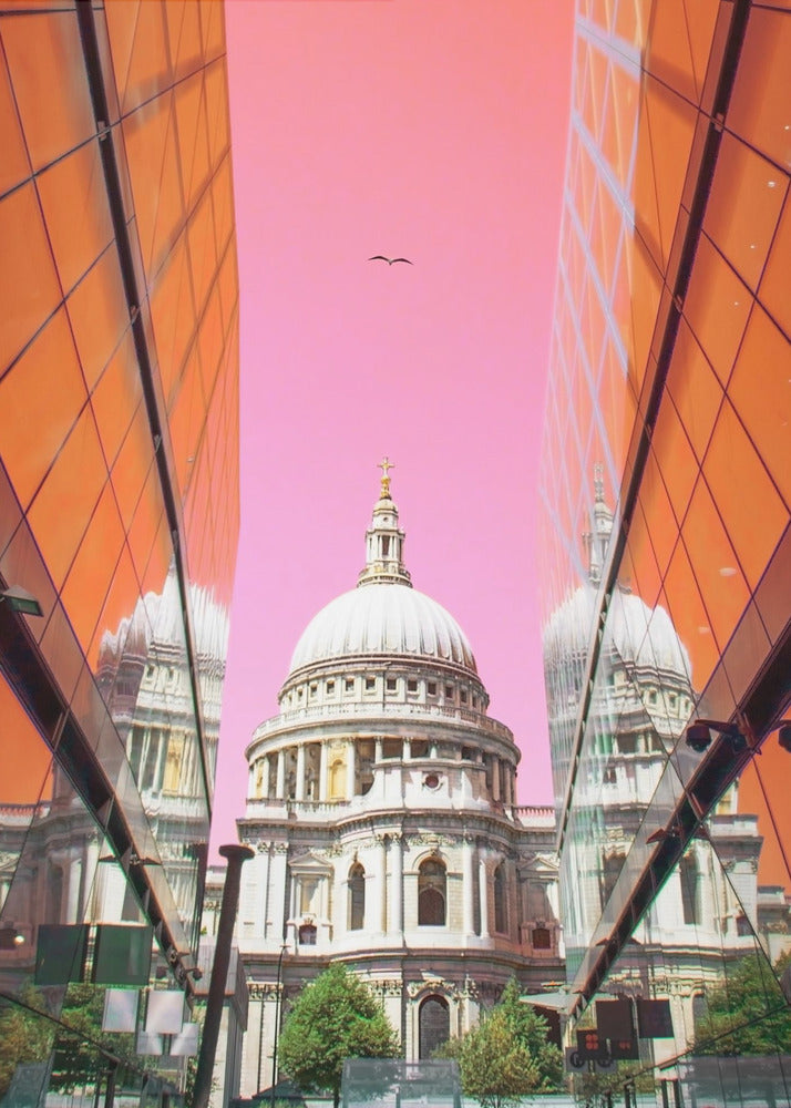 A low-angle, surrealist photograph of a classic white dome cathedral, framed perfectly between two modern orange glass buildings. The cathedral's reflection is visible on the buildings' surfaces against a vibrant, solid pink sky with a lone bird in flight. Poster