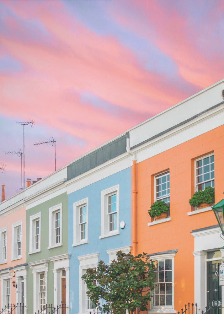 A row of colorful pastel townhouses in shades of orange, blue, green, and pink, viewed from a low angle against a dramatic, cloudy pink and purple sunset sky. Poster