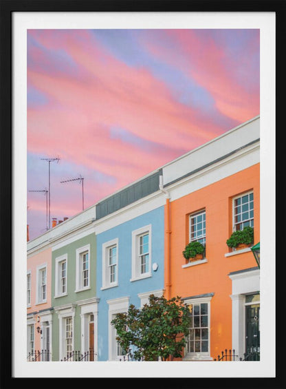 A row of colorful pastel townhouses in shades of orange, blue, green, and pink, viewed from a low angle against a dramatic, cloudy pink and purple sunset sky. Poster