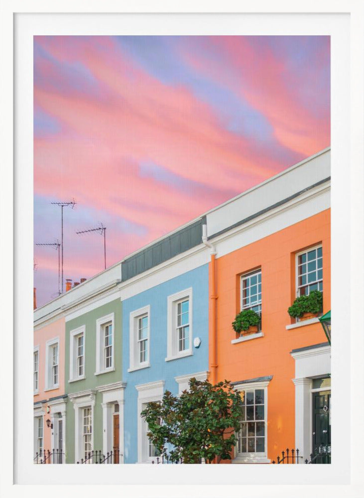 A row of colorful pastel townhouses in shades of orange, blue, green, and pink, viewed from a low angle against a dramatic, cloudy pink and purple sunset sky. Poster