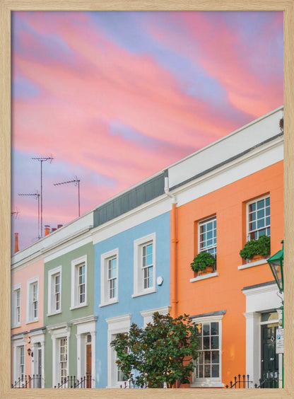 A row of colorful pastel townhouses in shades of orange, blue, green, and pink, viewed from a low angle against a dramatic, cloudy pink and purple sunset sky. Poster