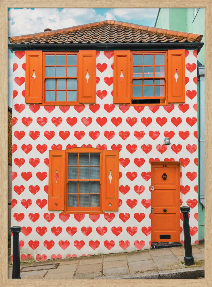 The front facade of a whimsical two-story house with white walls covered in a pattern of red hearts. The house has bright orange shutters on its windows and a matching orange front door, creating a vibrant and playful look against the heart-patterned background. Artwork