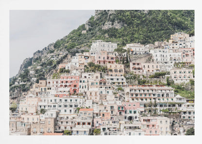 Photograph of the iconic cliffside village of Positano on the Amalfi Coast, showcasing a dense cascade of white, pink, and peach buildings down a lush green mountain under an overcast sky. The image is presented within a silver picture frame. Artwork
