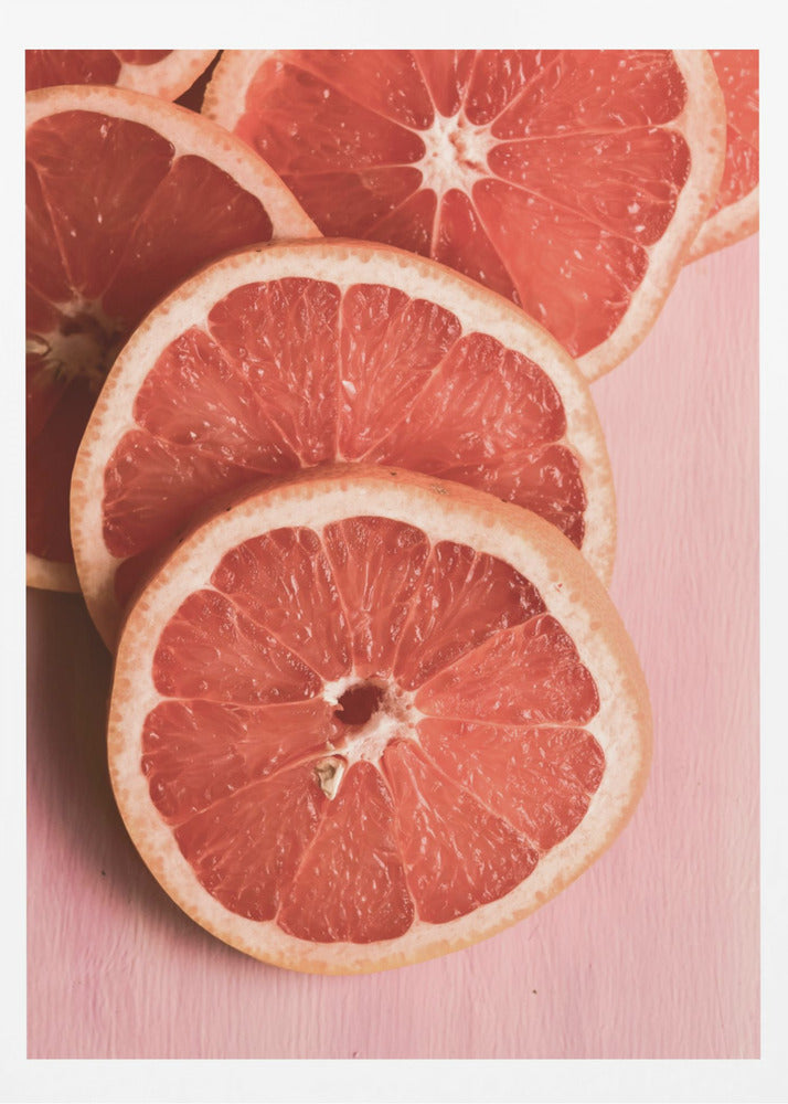 A close-up photograph of several overlapping slices of vibrant pink grapefruit arranged on a pale pink surface, enclosed within a simple black frame. Print
