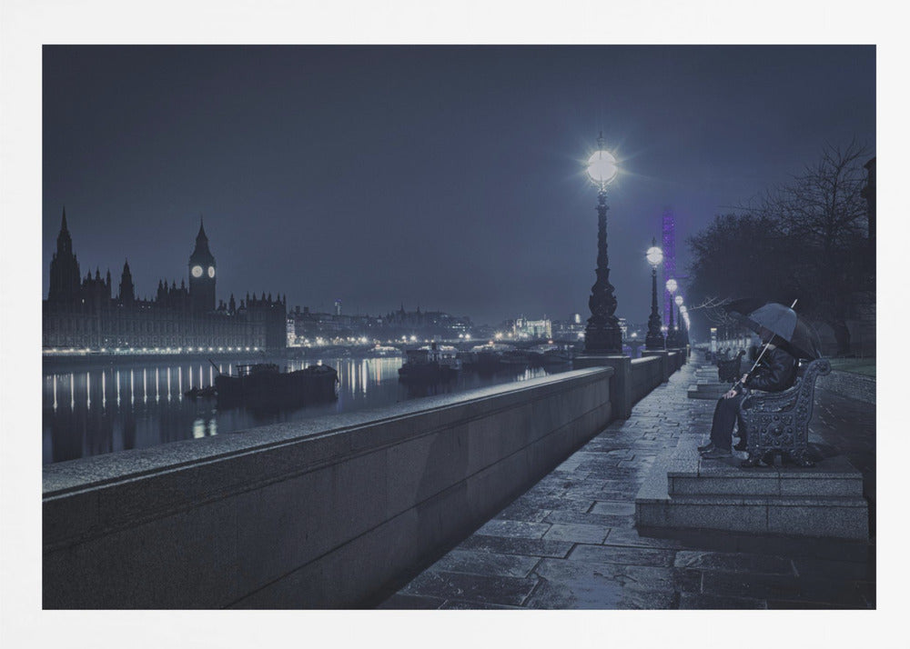 A moody, blue-toned night photograph of London. A solitary figure sits on a bench under an umbrella on a wet stone walkway along the River Thames, illuminated by vintage streetlights. Across the river, the iconic Houses of Parliament and Big Ben are lit up against the dark sky, their lights reflecting in the water. Poster