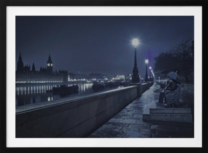 A moody, blue-toned night photograph of London. A solitary figure sits on a bench under an umbrella on a wet stone walkway along the River Thames, illuminated by vintage streetlights. Across the river, the iconic Houses of Parliament and Big Ben are lit up against the dark sky, their lights reflecting in the water. Poster