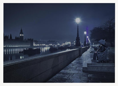 A moody, blue-toned night photograph of London. A solitary figure sits on a bench under an umbrella on a wet stone walkway along the River Thames, illuminated by vintage streetlights. Across the river, the iconic Houses of Parliament and Big Ben are lit up against the dark sky, their lights reflecting in the water. Poster