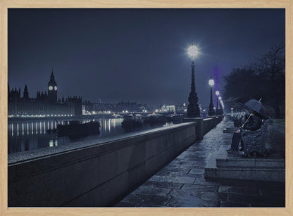 A moody, blue-toned night photograph of London. A solitary figure sits on a bench under an umbrella on a wet stone walkway along the River Thames, illuminated by vintage streetlights. Across the river, the iconic Houses of Parliament and Big Ben are lit up against the dark sky, their lights reflecting in the water. Poster