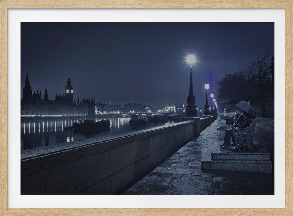 A moody, blue-toned night photograph of London. A solitary figure sits on a bench under an umbrella on a wet stone walkway along the River Thames, illuminated by vintage streetlights. Across the river, the iconic Houses of Parliament and Big Ben are lit up against the dark sky, their lights reflecting in the water. Poster