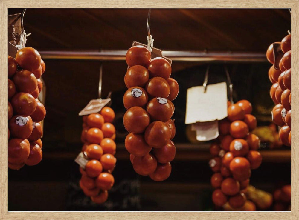 A close-up, warm-toned photograph of several bunches of ripe red tomatoes hanging from hooks in a row, likely at a market or in a pantry. The background is dark and out of focus, highlighting the vibrant produce. Poster