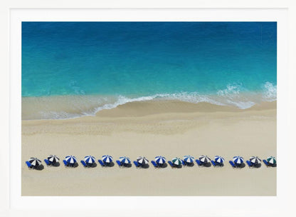 An aerial view of a pristine sandy beach with vibrant turquoise ocean waves gently lapping the shore. A long, neat row of blue and white striped beach umbrellas stands along the sand, creating a serene and orderly coastal scene, all enclosed within a silver frame. Artwork