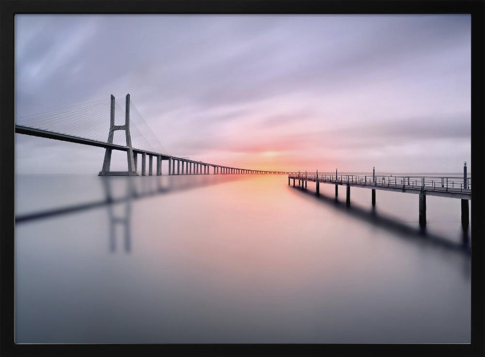 A serene long-exposure photograph of a modern cable-stayed bridge and a pier stretching over mirror-like water at sunset. The sky is filled with soft, streaky clouds in hues of pink and purple, reflected on the calm water's surface, all enclosed in a silver frame. Decor